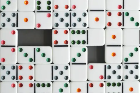 Wiele białych kostek do gry w domino z kolorowymi kropkami (zielonymi, czerwonymi, szarymi i pomarańczowymi) ułożonych w rzędy.