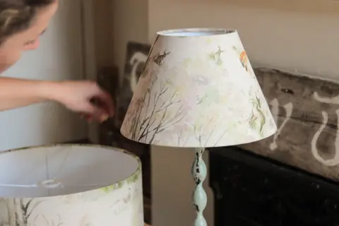Osoba tworzy abażur do lampy stojącej z motywem leśnych zwierząt.