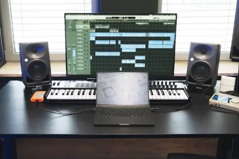 Studio do nagrywania muzyki: monitory studyjne, klawiatury MIDI, laptop i ekran z sekwencerem.