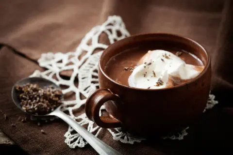 Una tazza di cioccolata calda senza cacao, con panna montata e lavanda. Un cucchiaio contiene lavanda secca.
