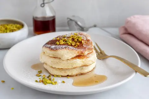Fluffiga japanska pannkakor toppade med pistagenötter och pudersocker, serverade med sirap.