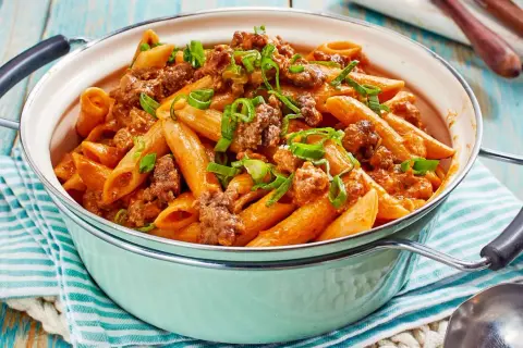 Herzhaftes One Pot Pasta mit Hackfleisch und einer cremigen Tomatensoße, garniert mit Frühlingszwiebeln.