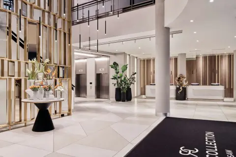 Eleganckie lobby hotelu Radisson Collection Hotel Warsaw z nowoczesnymi windami, recepcją i dekoracjami roślinnymi.