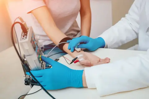 Lekarz bada przewodnictwo nerwowe pacjenta, podłączając elektrody do jego przedramienia.