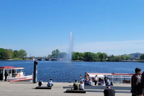 Ein sonniger Tag am Alstersee Hamburg. Menschen entspannen sich am Ufer, während die berühmte Fontäne in die Höhe schießt.