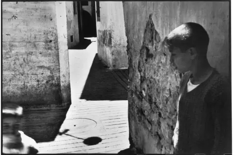 Un jeune garçon se tient dans une ruelle étroite, une ombre projetée sur le sol. Une scène typique des henri cartier bresson photos célèbres.