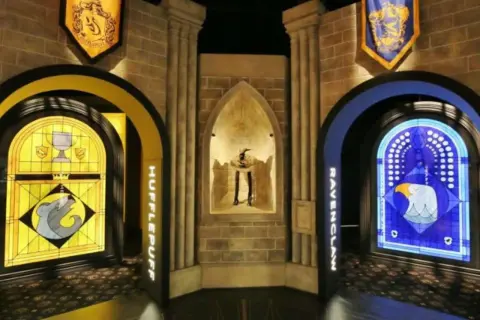 Wystawa Harry Potter: witraże Hufflepuff i Ravenclaw, a w centrum figura z kapeluszem.