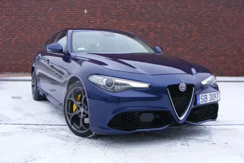 Niebieskie Alfa Romeo Giulia Veloce z żółtymi zaciskami hamulcowymi na tle ceglanej ściany, na śniegu.
