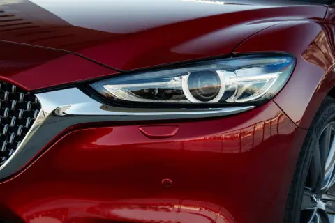 Błyszczący, czerwony lakier Mazda 6 Skyactiv odbija otoczenie. Widoczny fragment reflektora i chromowana atrapa.