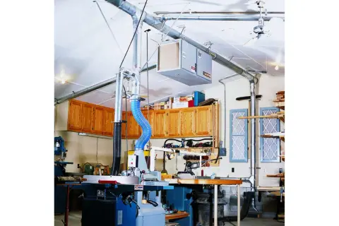 Atelier de menuiserie avec aspirateur à copeaux, tuyauterie et armoires en bois.