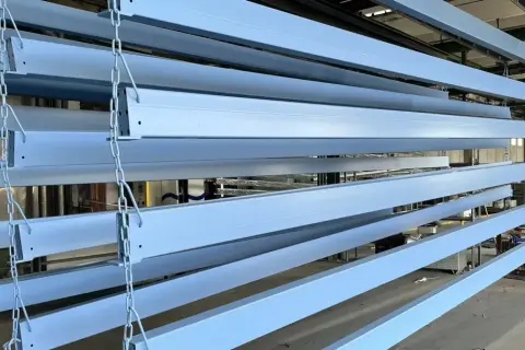 Profili in ferro azzurro appesi a catene, pronti per essere verniciati o dopo aver subito un processo di smerigliare ferro.