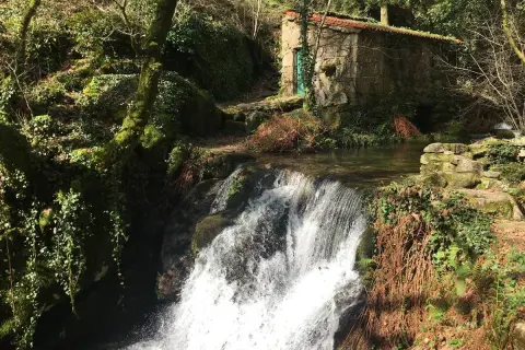 Cascada en el parque natural Monte Aloia, con una pequeña casa de piedra y vegetación exuberante.