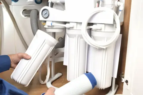 Montaż filtra do wody: ręce trzymają nowe wkłady i obudowę systemu odwróconej osmozy pod zlewem.