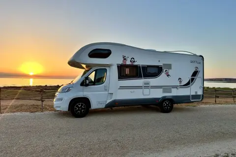 Autocaravana blanca aparcada junto al mar al atardecer. ¡La aventura de **Sicilia en autocaravana** comienza!