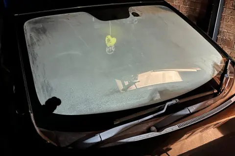 En frostig vindruta på en bil. En gul hjärtformad doftgran hänger från backspegeln.