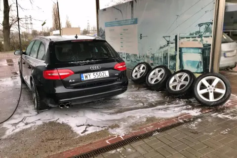 Czarny Audi na myjni bezdotykowej, obok cztery koła. Poznaj myjnia bezdotykowa triki, by Twój samochód lśnił!