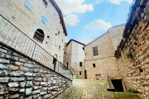 Antica via acciottolata a Caldarola, Marche, con edifici in pietra e cielo azzurro.