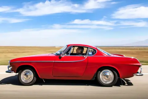 Irv Gordon kör sin röda Volvo P1800 över ett öppet fält under en klarblå himmel.