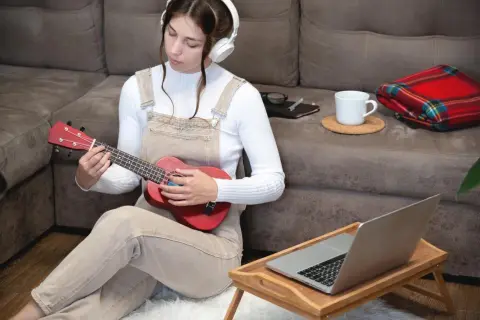 Dziewczyna w słuchawkach uczy się grać na ukulele, zastanawiając się, ile trwa nauka gry na gitarze.