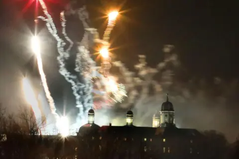 Feuerwerk über Bergisch Gladbach. Farbenfrohe Raketen erleuchten den Nachthimmel über einem historischen Gebäude mit Kuppeln.