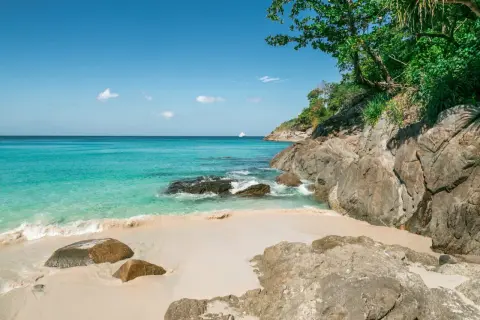 Piękne plaże Phuket z turkusową wodą, piaszczystym brzegiem i skalistym wybrzeżem. Na horyzoncie biała łódź.