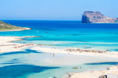 Rajska plaża z turkusową wodą i skalistą wysepką w oddali. Czy to Rodos czy Kreta? Trudno odróżnić ten cud natury.