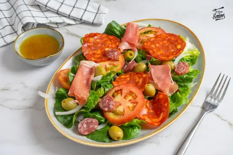 Una fresca ensalada catalana con lechuga, tomate, aceitunas, chorizo, salchichón y jamón serrano.