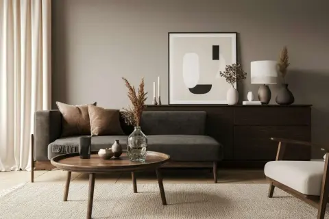 Ein Wohnzimmer mit dunklem Sofa, braunen Kissen und einem runden Holztisch. Die Frage, welche Farbe passt zu Schwarz, wird hier mit warmen Erdtönen beantwortet.