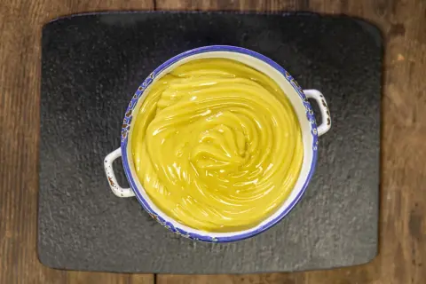 Una ciotola di cremosa crema pasticcera vegana, con un vortice lucido al centro, pronta per farcire dolci.