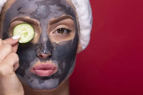 Donna con maschera viso all'argilla e fetta di cetriolo sull'occhio. La maschera viso a cosa serve? A purificare e rinfrescare la pelle.