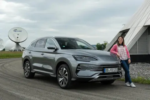 Mujer sonríe junto a un BYD Seal U, disfrutando del dm-i comfort en un día nublado, con antenas parabólicas de fondo.