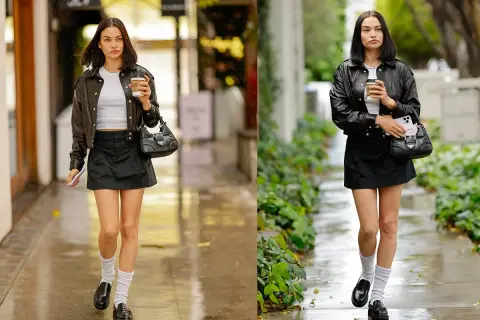 Moda urbana con giacca di pelle, minigonna nera, mocassini e calzini bianchi. La ragazza cammina con un caffè in mano.