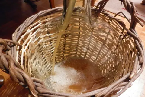 Płyn przelewany do szklanej butli w wiklinowym koszu, tworząc pianę.