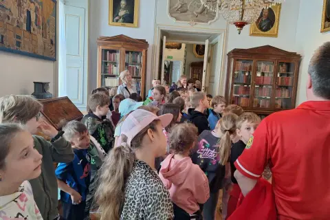 Wycieczka szkolna w Pałacu w Nieborowie. Dzieci słuchają przewodnika wśród zabytkowych mebli i obrazów.