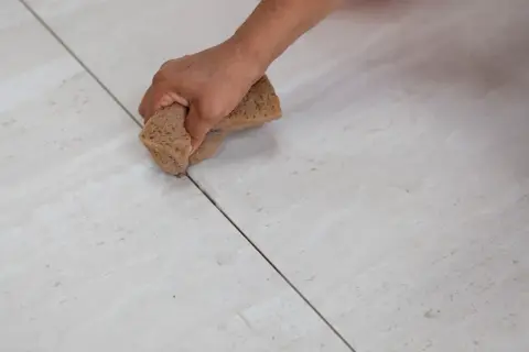 Main d'une personne nettoyant le joint carrelage avec une éponge.