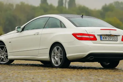 Biały w212 coupe z polskimi tablicami rejestracyjnymi stoi na mokrej nawierzchni.