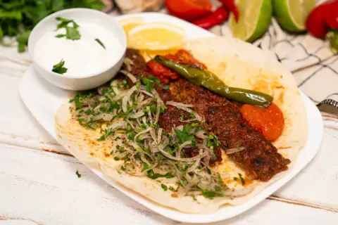 Domowy kebab z mięsem, cebulą, pietruszką, pomidorami i sosem jogurtowym na placku.