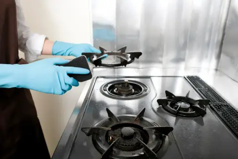 Mani con guanti azzurri puliscono fornelli a gas con una spugna. Guida su come pulire i fornelli del gas per una cucina splendente.
