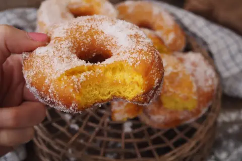 En hand håller en sockerdränkt munk, perfekt för ett hembakat donuts recept.