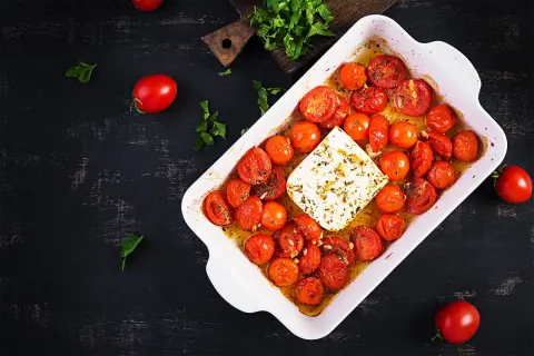 Tomates cerises au four, tendres et juteuses, baignant dans leur jus avec un bloc de feta crémeuse. Un délice simple et savoureux.