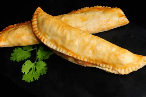 Dos empanadas de salmón doradas y crujientes, con un toque de cilantro fresco sobre fondo negro.