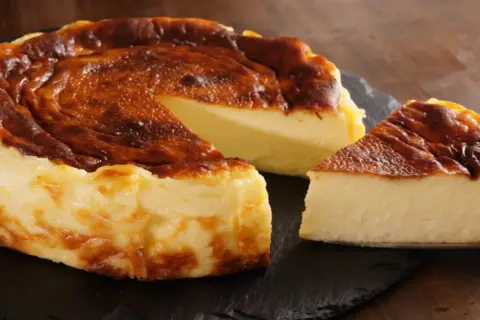 Pyszny, lekko przypieczony sernik na czarnej desce. Nawet jeśli sernik kcal kusi, warto spróbować!