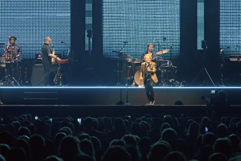 Ein Musiker mit goldenem Sakko singt auf der Bühne, umgeben von seiner Band. Ein Konzert von Simply Red in Stuttgart.