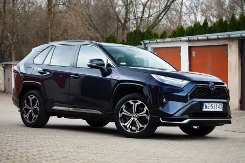 Ciemnoniebieski Toyota RAV4 Hybrid, często chwalony w toyota rav4 opinie, zaparkowany przed garażami.