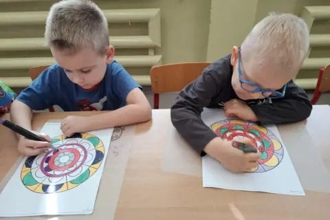 Dwóch chłopców z zapałem koloruje swoje mandale.
