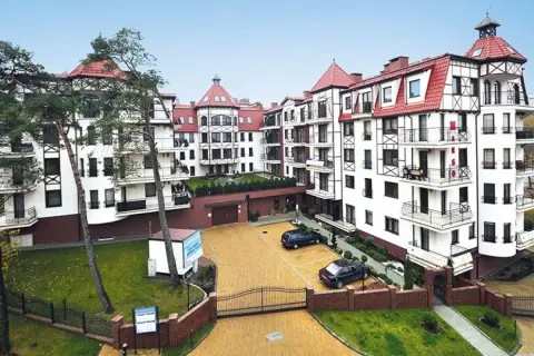 Elegancki budynek w stylu alpejskim, przypominający Continental Hotel Krynica, z białymi fasadami, czerwonymi dachami i drewnianymi elementami.