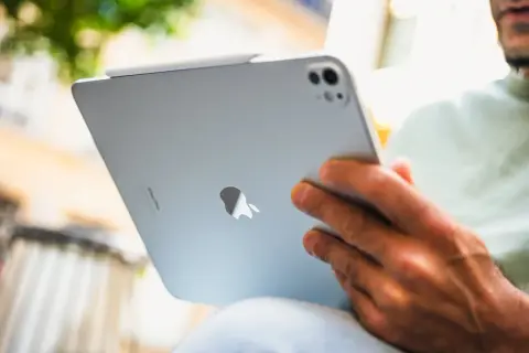 Un homme est assis dehors, profitant d'un moment pour lire sur son iPad.