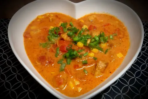 Pyszna zupa gyros z kawałkami kurczaka, kukurydzą i pomidorami, posypana szczypiorkiem.