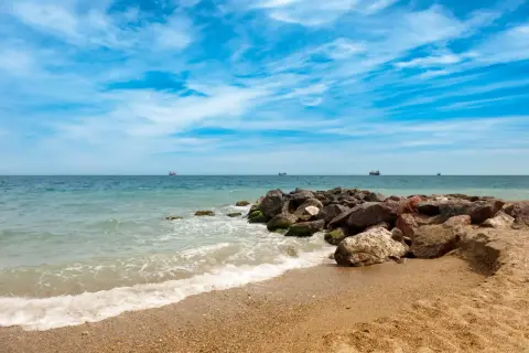 Olas rompiendo en la arena dorada de la playa Quitapellejos. El mar turquesa se extiende hasta el horizonte, con barcos navegando. ¡Un lugar ideal para relajarse!