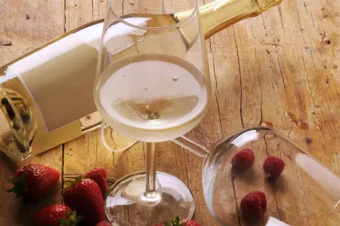 Butelka i kieliszek pełne musującego płynu, obok truskawki i maliny. To jest prosecco, idealne na letnie popołudnie.